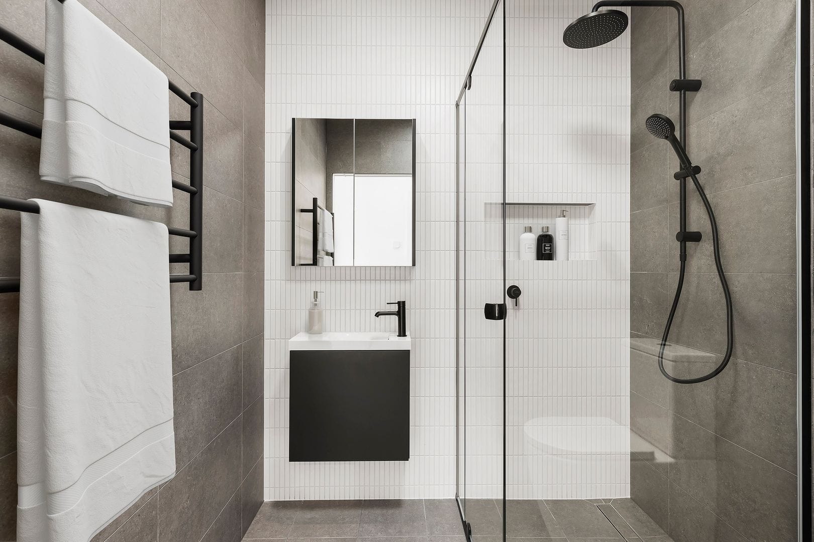 Contemporary bathroom with grey tiles, black fixtures, glass shower enclosure, and wall-mounted vanity.