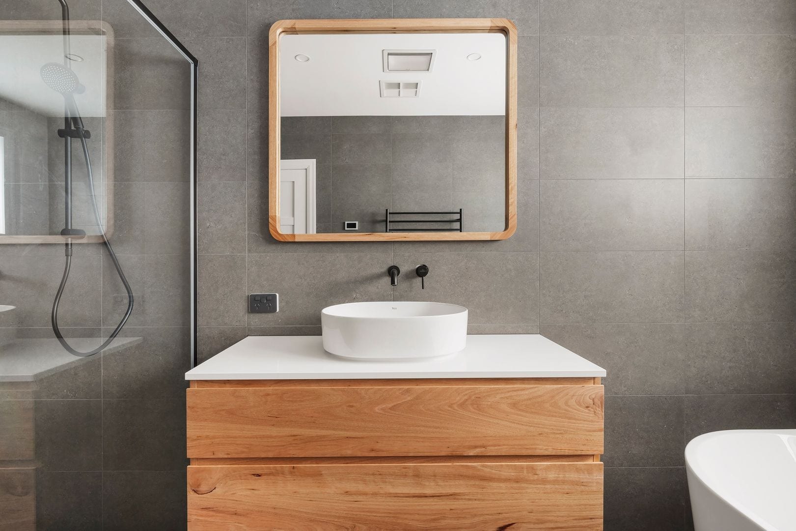 Modern bathroom with wooden vanity, vessel sink, large mirror, and glass shower enclosure.