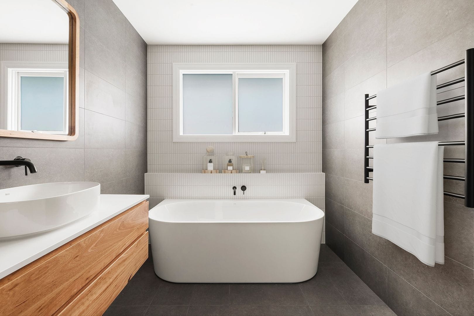 Modern bathroom with freestanding tub, wooden vanity, and black fixtures.