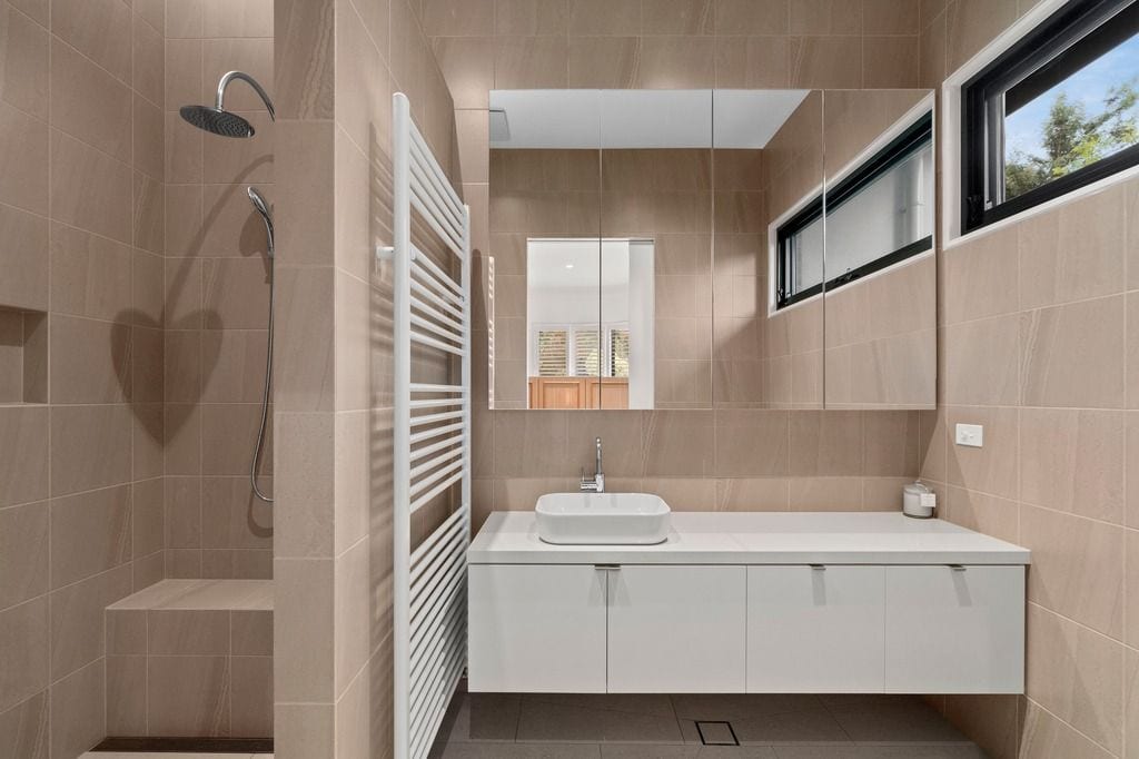 Modern bathroom with beige tiles, walk-in shower, white floating vanity, and large mirror.