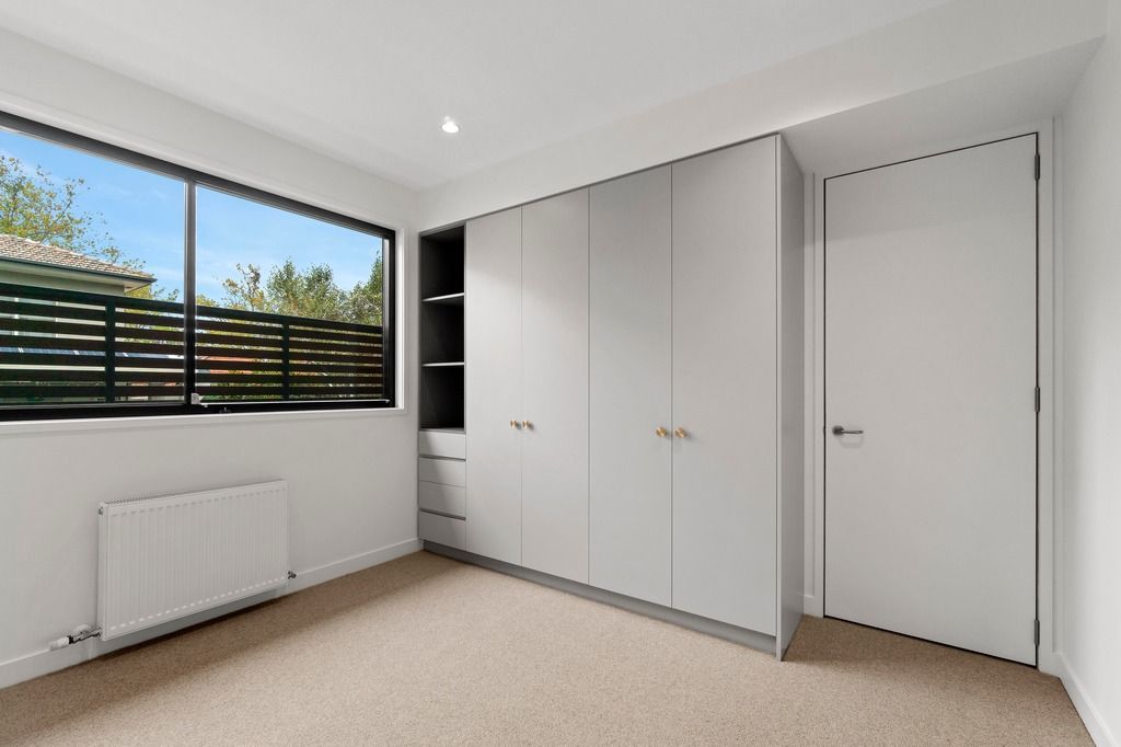 Bedroom with large window, radiator heater, built-in wardrobe, and beige carpet flooring.
