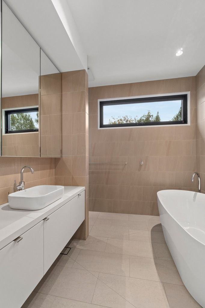 Modern bathroom with freestanding bathtub, white countertop, and beige tiles.