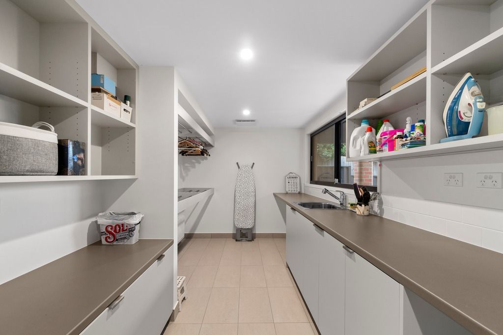 Modern laundry room with shelves, ironing board, sink, and cleaning supplies.