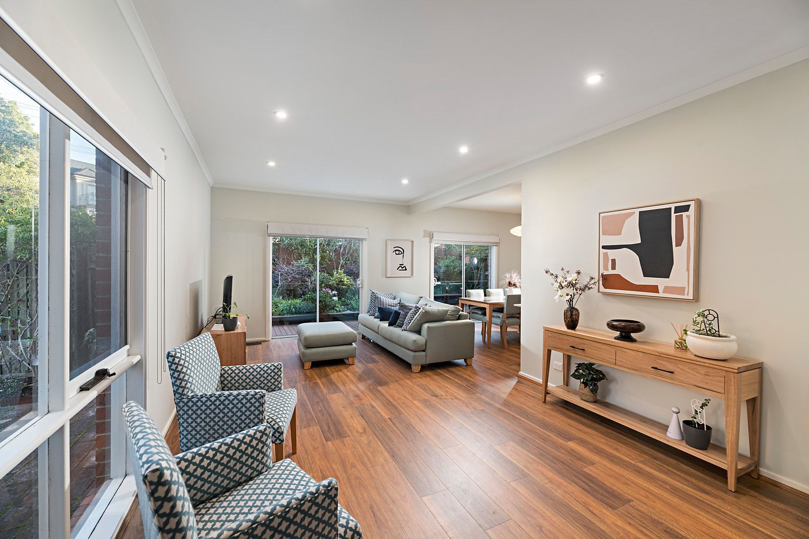 Renovated living room with wooden flooring, modern furniture, and sliding glass doors leading to a garden.