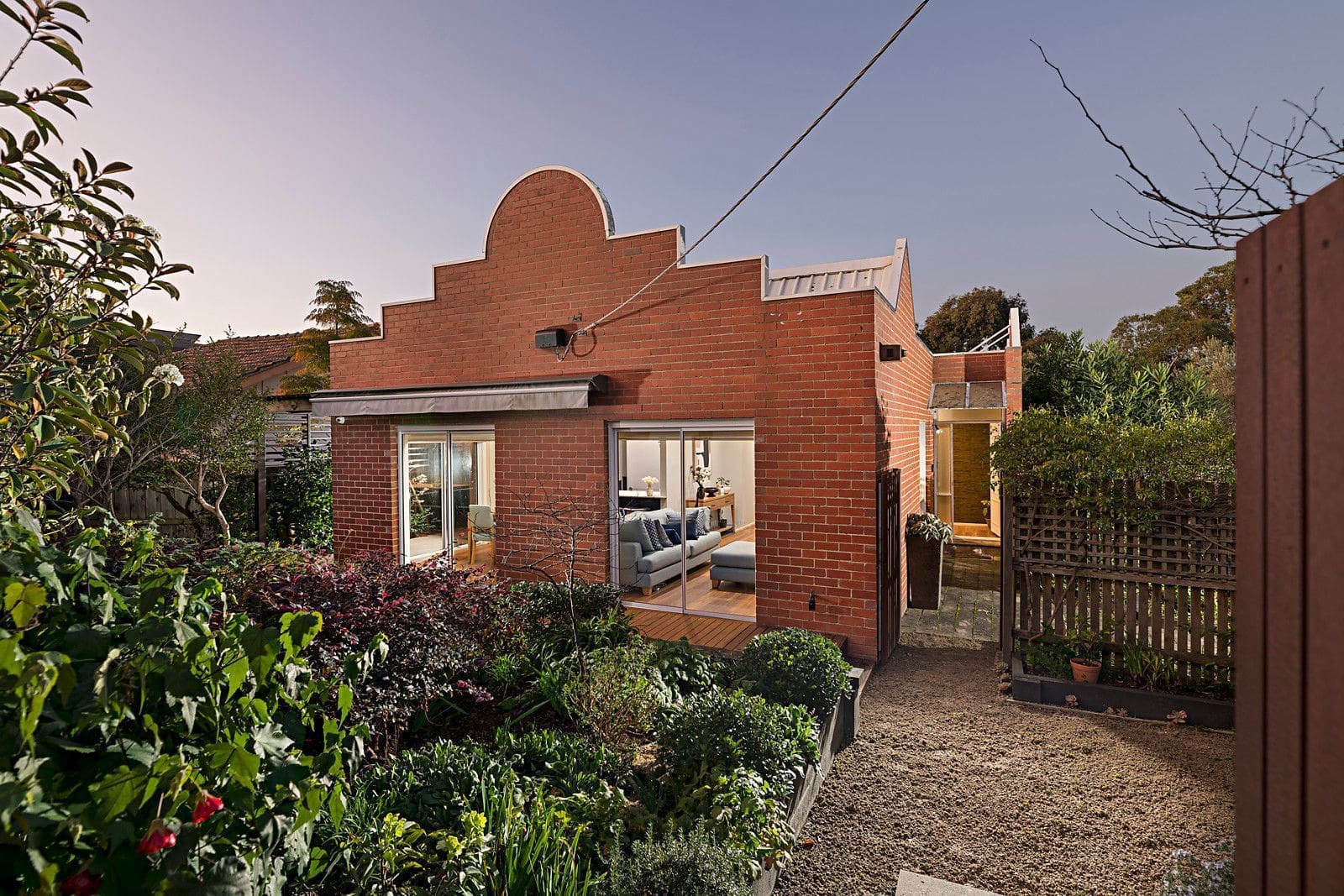 Red brick house with stepped gable design, garden, and visible modern interior through sliding glass doors