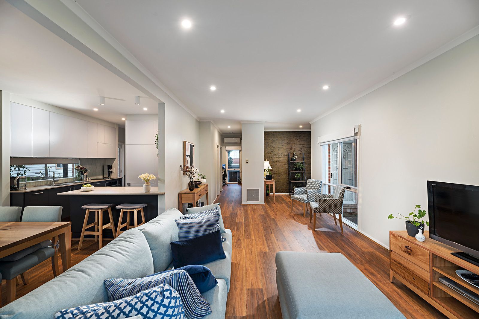 Open-plan living area with kitchen, dining table, sofa, TV stand, and modern decor.