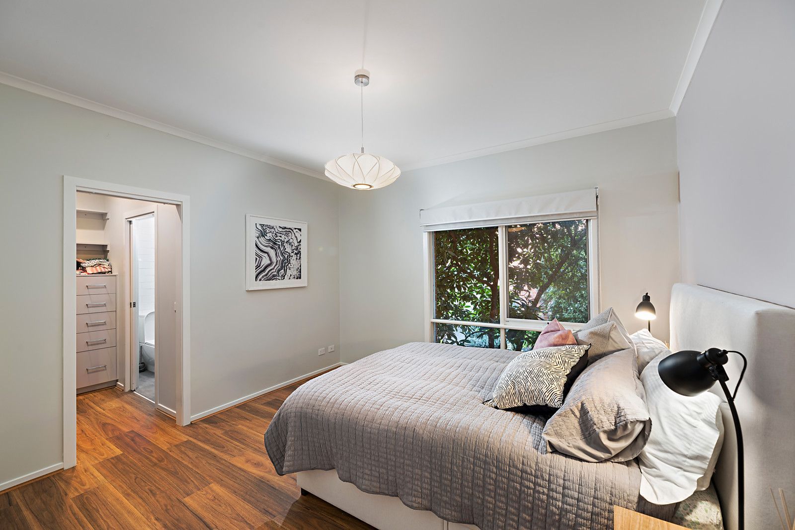 Renovated bedroom with wooden flooring, gray bedding, large window, and en-suite bathroom.