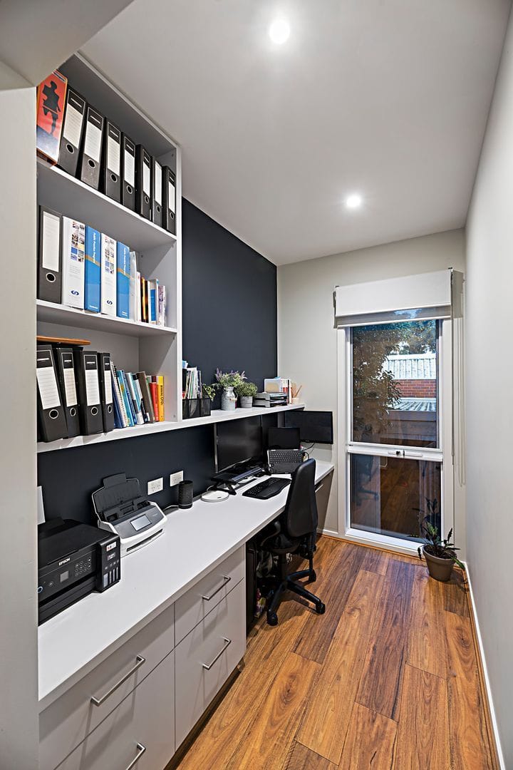 Home office with organized shelves, dual monitors on a long desk, and wooden flooring.